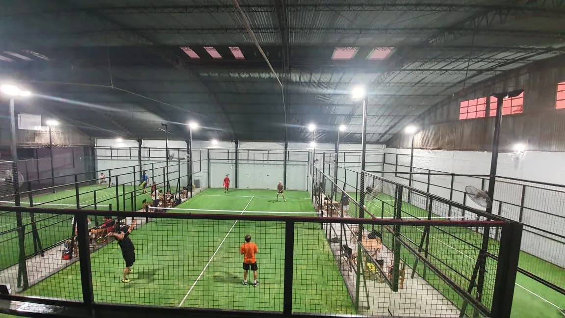 El galpón de Paddock de noche con las canchas de césped iluminadas y gente jugando