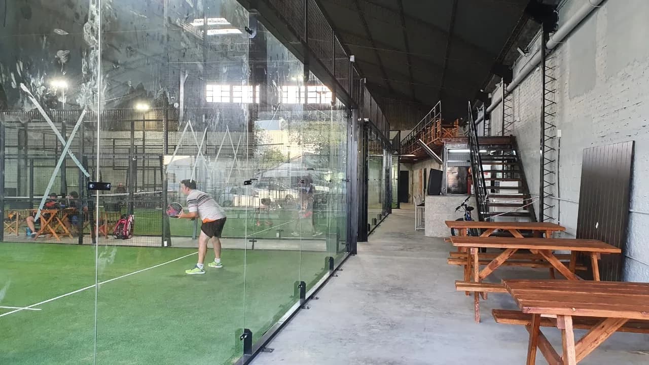 Mesas de madera en el pasillo de Paddock, al lado de una cancha de vidrio donde alguien está jugando