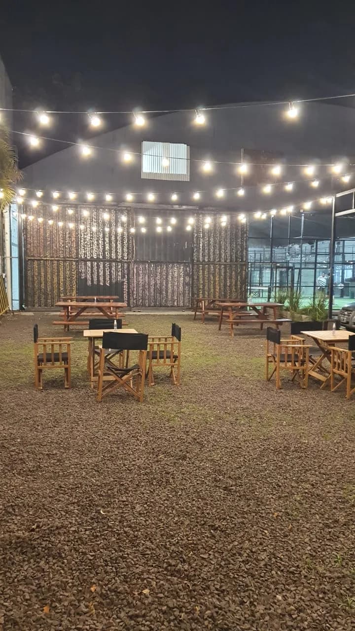 El patio de noche, con guirnaldas de lamparitas, mesas de madera y sillas de director